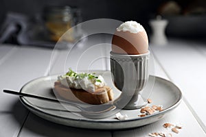 Fresh soft boiled egg in cup and sandwich on white wooden table