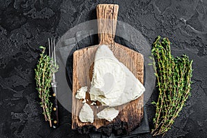 Fresh Soft goat cheese on a cutting board with thyme. Black background. Top view