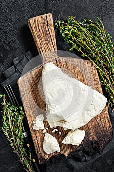 Fresh Soft goat cheese on a cutting board with thyme. Black background. Top view