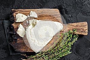 Fresh Soft goat cheese on a cutting board with thyme. Black background. Top view