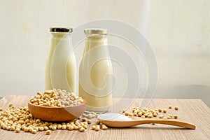 Fresh soybean seeds in brown wooden bowl with sugar in spoon and two bottles of soy milk on the table