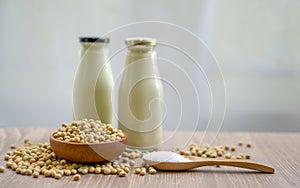 Fresh soybean seeds in brown wooden bowl with sugar in spoon and two bottles of soy milk on the table