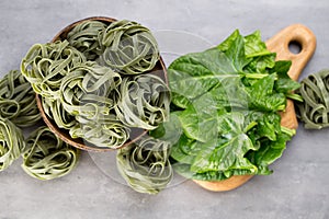 Fresh spinach with green pasta on a gray background.