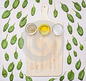 Fresh spinach leaves have been laid out around a vintage white cutting board, frame, space for text, top view