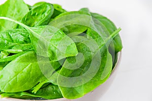 Fresh spinach leaves with water drops in ceramic bowl on thw white wooden background. Selective focus. Space for text