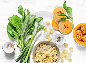 Fresh spinach, pumpkin, orekiette pasta-ingredients for a vegetarian lunch on a light background, top view. Healthy, diet food