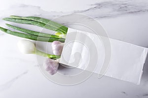 Fresh spring onions and garlic in the white paper bag on the marble surface