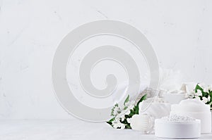 Fresh spring organic spa cosmetics products with small white flowers and green leaves on white wood background, copy space.
