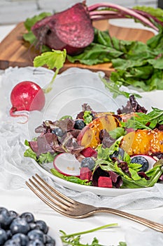 Fresh spring salad with rucola, lettuce, blueberries, radish, beet and slices of peach. White background with free text space