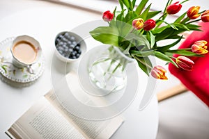 Fresh spring tulips in glass vase and a cup of coffee with a book