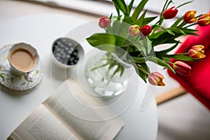 Fresh spring tulips in glass vase and a cup of coffee with a book