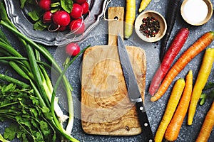 Fresh spring vegetables around wooden cutting board with kitchen knife for vegetarian cooking