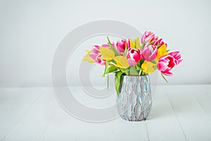 Fresh spring yellow and pink tulips bouquet in blue vase on white wooden table with white background. Festive flowers for mother`