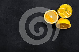 Fresh squeezed orange juice in glass near half cut oranges on black background top view copy space