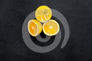 Fresh squeezed orange juice in glass near half cut oranges on black background top view copy space