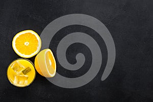 Fresh squeezed orange juice in glass near half cut oranges on black background top view copy space