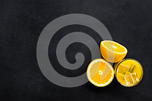 Fresh squeezed orange juice in glass near half cut oranges on black background top view copy space