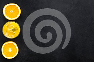 Fresh squeezed orange juice in glass near half cut oranges on black background top view pattern copy space