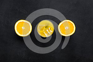 Fresh squeezed orange juice in glass near half cut oranges on black background top view pattern copy space