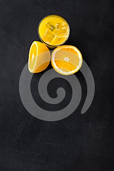 Fresh squeezed orange juice in glass near half cut oranges on black background top view space for text