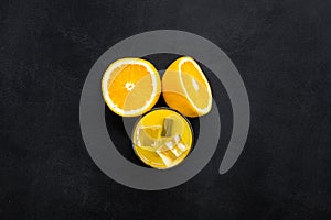 Fresh squeezed orange juice in glass near half cut oranges on black background top view space for text