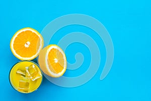 Fresh squeezed orange juice in glass near half cut oranges on blue background top view copy space