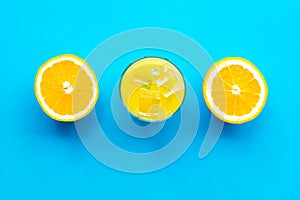 Fresh squeezed orange juice in glass near half cut oranges on blue background top view pattern copy space