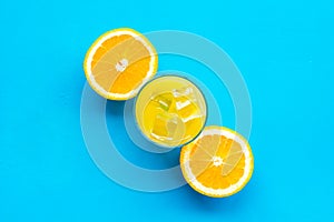 Fresh squeezed orange juice in glass near half cut oranges on blue background top view pattern copy space