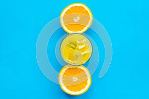 Fresh squeezed orange juice in glass near half cut oranges on blue background top view pattern copy space
