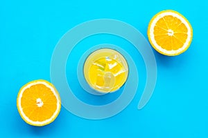 Fresh squeezed orange juice in glass near half cut oranges on blue background top view pattern copy space