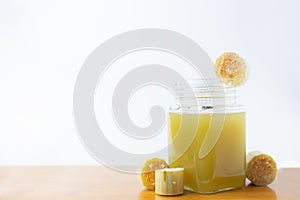 Fresh squeezed sugar cane juice in clear glass with cut pieces cane on white background