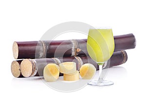 Fresh squeezed sugar cane juice in glass with cut pieces cane on white background