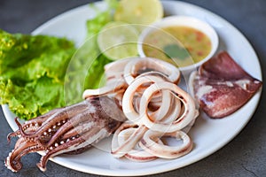 Fresh squid cooked boiled with lettuce vegetable salad lemon and seafood sauce on table background, squid rings on white plate