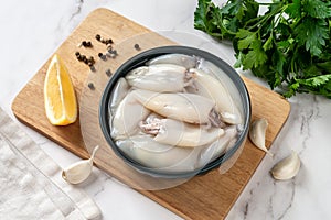 Fresh squid tubes in a bowl. Small calamary fillet and parsley prepared for cooking. Raw squid molluscs as ingredient for low