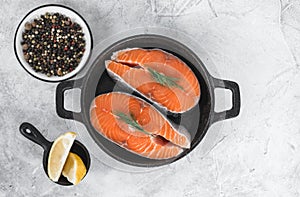 Fresh steaks of red salmon fish with spices, herbs and lemon in a black pan