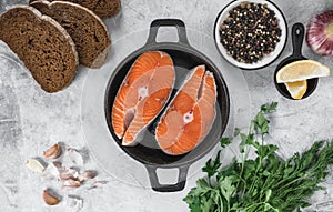 Fresh steaks of red salmon fish with spices, herbs and lemon in a black pan