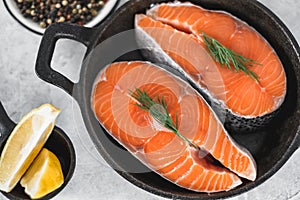 Fresh steaks of red salmon fish with spices, herbs and lemon in a black pan