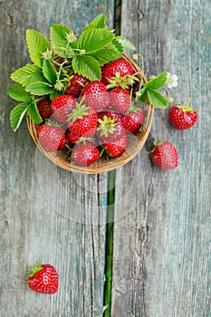 Fresh strawberries in a basket on rustic wooden background top view