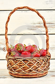 Fresh strawberries in basket on white wooden background.