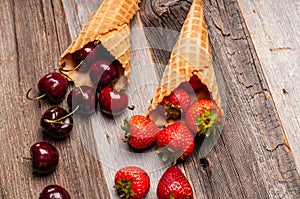 Fresh strawberries and cherries in waffle cones on wooden table