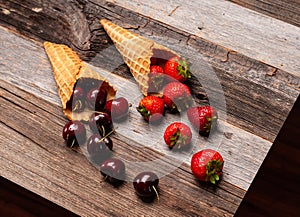 Fresh strawberries and cherries in waffle cones on wooden table