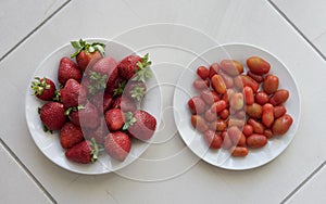 Fresh strawberries and fresh small tomatoes served on a white plate and in grey natural ceramic background. Fruits and ve