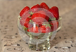 Fresh strawberries in glass bowl on table. Ripe strawberry closeup. Sweet summer harvest. Juicy dessert. Healthy food.