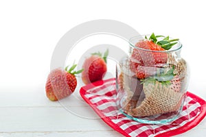 Fresh strawberries in glass jar on white wood background with se