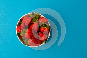 Fresh strawberries and green leaf in bowl isolated on blue background