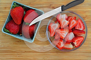 Fresh strawberries in a market basket with sliced strawberries to the side in a glass bowl. Top view