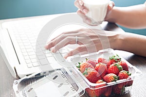 Fresh strawberries on office desk with woman drinking milk, Heal