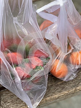 Fresh strawberries in a plastic bags on a wooden bench. Raindrops on a surface