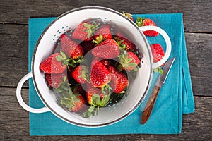 Fresh strawberries in rustic colander on wooden table