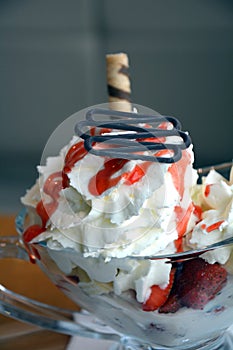 Fresh strawberries and vanilla ice cream with whipped cream on a glass bowl.